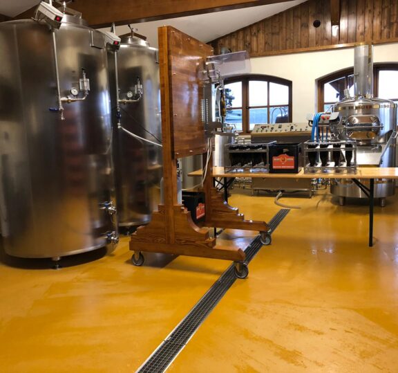 Pardoseală din beton poliuretanic, galbenă în fabrică de producție cu tancuri din inox și rigolă de inox pentru drenaj.