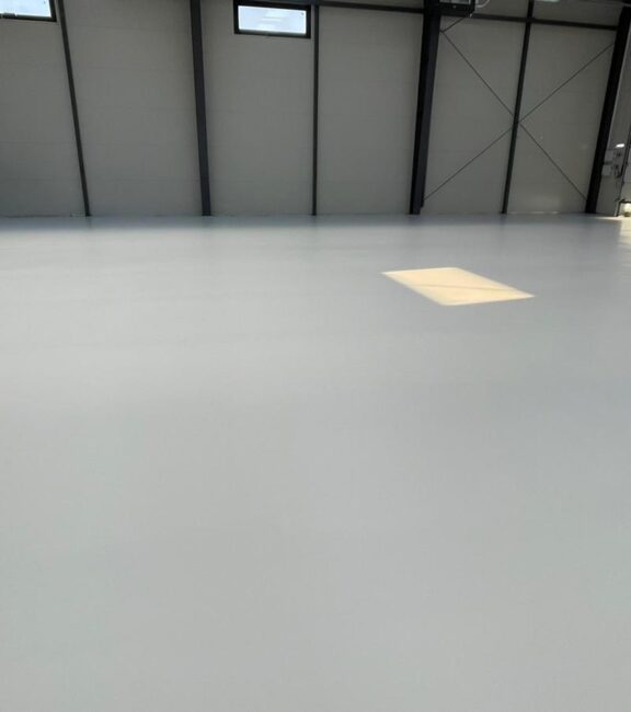 Pardoseală epoxidică mată, gri într-un depozit industrial nou cu structură metalică