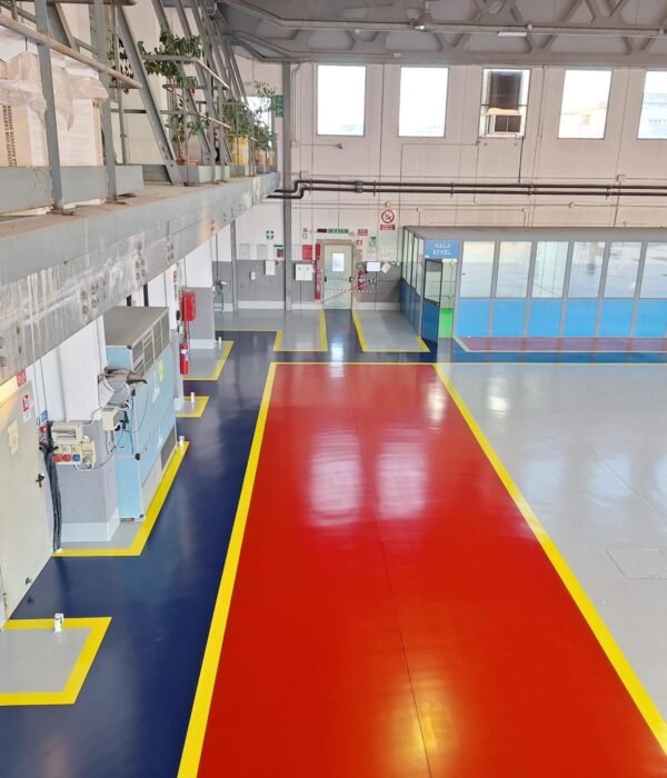 Pardoseală epoxidică industrială multicoloră cu zone roșii, gri și bleumarin într-o hală de producție.