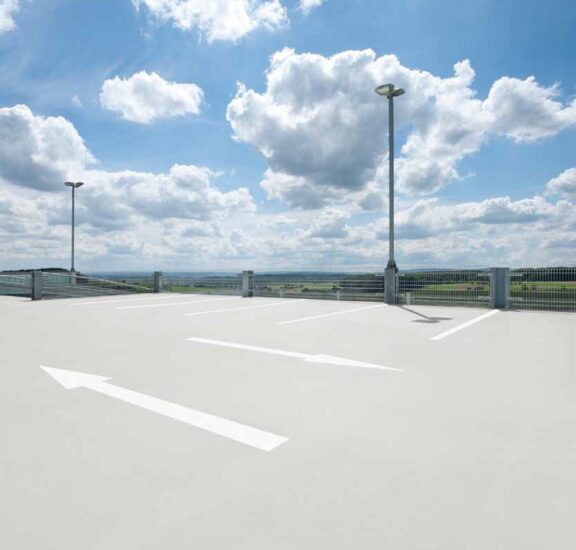 Pardoseală din rășină poliuretanică pentru parcare auto exterioară pe acoperiș, cu marcaje albe direcționale.